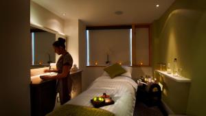 a woman standing next to a bed in a room at Lifehouse Spa And Hotel in Frinton-on-Sea