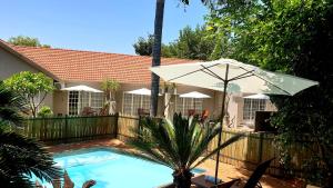 a swimming pool with an umbrella next to a house at Khayamanzi Guesthouse in Hartbeespoort