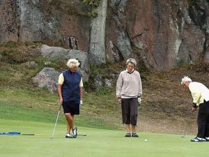 drie oudere mensen die golfen op een golfbaan bij 8 person holiday home in Gudhjem in Gudhjem