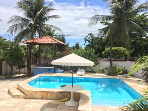 uma piscina com um guarda-sol e uma mesa com em Beach House Paracuru B&B - cama e café em Paracuru