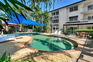 a swimming pool with a blue umbrella in front of a house at Cairns Reef Apartments & Motel in Cairns