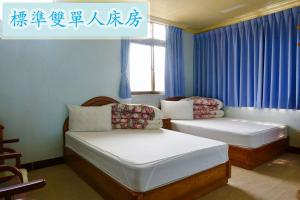 2 Betten in einem Zimmer mit blauen Vorhängen in der Unterkunft Yi Mei Hotel in Jinshan