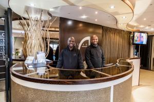 Dois homens à frente de um balcão numa loja. em Aquarius Luxury Suites em Bloubergstrand