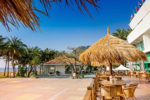 een patio met tafels en stoelen en een rieten parasol bij Sunset Beach Resort in Kaohsiung