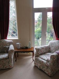 a living room with two chairs and a table and windows at Ambles in Northampton