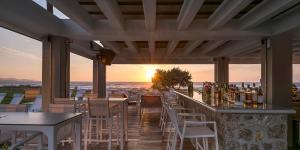 een bar met tafels en stoelen en de oceaan bij zonsondergang bij Thalassa Suites in Almiros strand