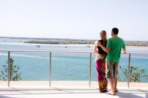 Una pareja de pie en un balcón con vistas al agua en Silvershore Apartments on the Broadwater en Gold Coast