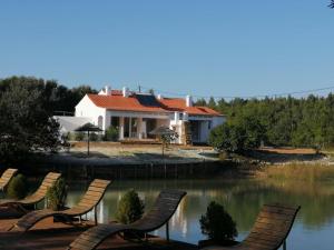 a house with chairs in front of a lake at Amor de Crianca in São Teotónio