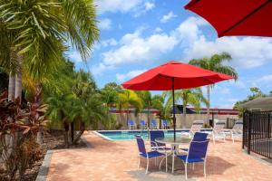 una mesa con sillas y una sombrilla roja junto a una piscina en Super 8 by Wyndham Bradenton Sarasota Area en Bradenton