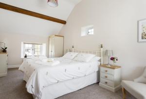 a white bedroom with a white bed and a chair at Alysas Cottage in Chipping Norton
