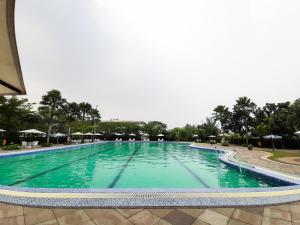 a large swimming pool with green water and umbrellas at Minimalist and Stylish Studio No Kitchen Apartment at Aeropolis Residence By Travelio in Tangerang +6 photos