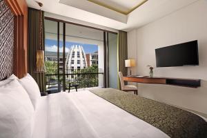 a hotel room with a bed and a desk and a balcony at Golden Tulip Jineng Resort Bali in Kuta