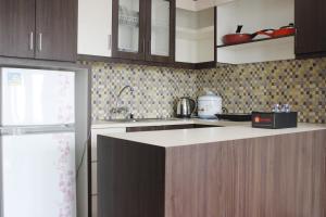 Modern Studio Room at Tamansari La Grande Apartment By Travelio في باندونغ: مطبخ بدولاب خشبي ومغسلة وثلاجة