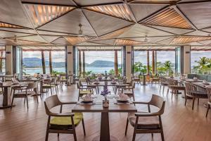 a dining room with tables and chairs and windows at Oceanfront Beach Resort - SHA Extra Plus in Patong Beach