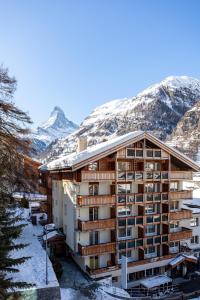 un hôtel dans la neige avec des montagnes en arrière-plan dans l'établissement Hotel Holiday, à Zermatt