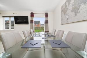 uma sala de jantar com uma mesa de vidro e cadeiras brancas em London Heathrow Living Holywell Serviced Houses - 3 and 4 bedrooms By Ferndale em Stanwell