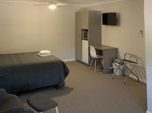 a bedroom with a bed and a desk and a kitchen at Mudgee Vineyard Motor Inn in Mudgee