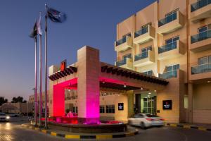 a building with a pink building with cars in front of it at Millennium Central Al Mafraq in Abu Dhabi