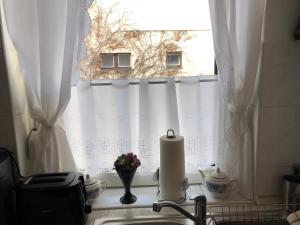 eine Küchenspüle mit einem Fenster mit weißen Vorhängen in der Unterkunft Centrum 2 Apartmanok in Hévíz