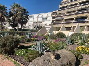 un jardin en face d'un grand bâtiment dans l'établissement BAGATELLE NATURISTE HELIOPOLIS clim ascenseur vue mer parking privé, au Cap d'Agde