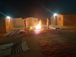 a group of people standing around a fire at night at Sahara Peace camp in Zagora