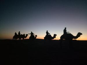 Eine Gruppe von Menschen, die bei Sonnenuntergang in der Wüste auf Pferden reiten in der Unterkunft Sahara Peace camp in Zagora