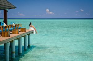 a woman sitting on a dock in the water at Summer Island Maldives Resort in North Male Atoll