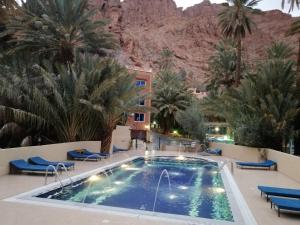 a pool in a resort with palm trees and a mountain at Auberge Camping Atlas in Tinerhir