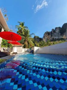 a swimming pool with a red umbrella and palm trees at Aonang Lodge - SHA in Ao Nang Beach