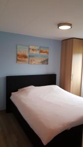 a bedroom with a white bed with three paintings on the wall at Vakantiewoning Koegras in Julianadorp