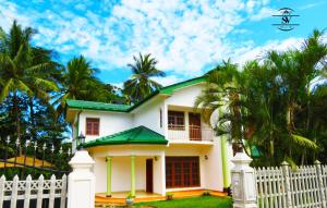 a white house with a white fence and palm trees at Stream View Family Resort in Dambulla