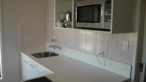 a kitchen with a microwave, sink, and dishwasher at Manukau Motor Lodge in Auckland