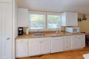 uma cozinha com armários brancos, um lavatório e duas janelas em 103 - Sea Cottage em St. Pete Beach