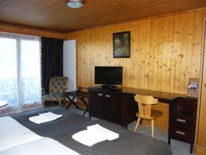 a bedroom with a bed and a desk with a television at Bellevue Bären Hotel & Restaurant in Krattigen