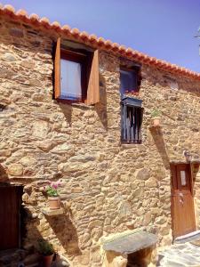 ein Steinhaus mit zwei Fenstern und einer Bank in der Unterkunft REFÚGIO DO RAPOSO/CASA DENEB (CC) in Montes da Senhora