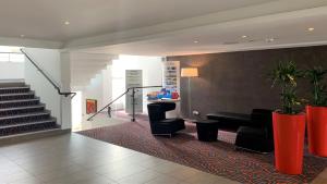 a lobby with black chairs and a stair case at Holiday Inn Lille Ouest Englos, an IHG Hotel in Englos
