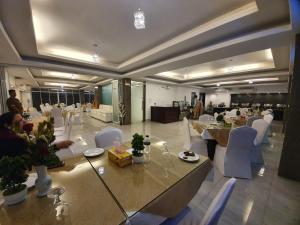 Habitación grande con mesas, sillas blancas y personas. en Aristocrat Inn en Dhaka