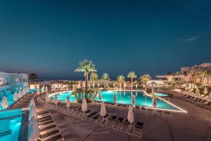 a resort with a pool with chairs and palm trees at Mitsis Rodos Village in Kiotari