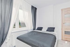 a white bedroom with a bed and a window at Jantar Apartamenty - Willa Jałowcowa in Grzybowo