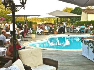 a swimming pool with people sitting around a restaurant at L'Hôtel du Périgord in Aubeterre-sur-Dronne