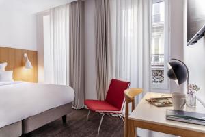パリにある9ホテル レピュブリックのベッド、デスク、赤い椅子が備わるホテルルームです。