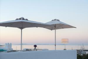 two white umbrellas on a beach with the ocean at Kanale's Rooms & Suites in Naousa