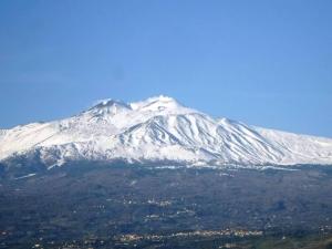 a snow covered mountain with a city in front of it at Casa EtnaparadisoTaormina- PiedimonteEtneo in Piedimonte Etneo
