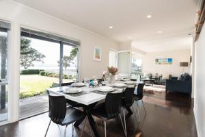une salle à manger avec une table, des chaises et une grande fenêtre dans l'établissement Wairangi Beach Cottage - Paihia Beach House, à Paihia