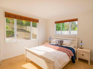 a white bedroom with a bed and two windows at Seaview Serenity- Whitianga Holiday Home in Whitianga