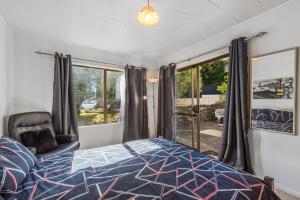 a bedroom with a bed and a chair and windows at Sandcastles on Tay - Mt Maunganui Holiday Home in Mount Maunganui