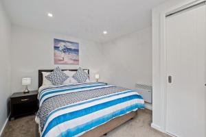 a white bedroom with a bed with blue and white stripes at Queenstown Lake Views - Downstairs Apartment in Queenstown