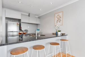 a kitchen with wooden stools and a counter top at Sunrise, Seaviews and BBQs-Papamoa Beach Apartment in Papamoa