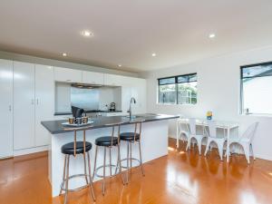 a kitchen with white cabinets and a bar with stools at Cheviot's Hideaway - Mangawhai Heads Holiday Home in Mangawhai