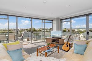 a living room with a couch and a tv and windows at Sunrise, Seaviews and BBQs-Papamoa Beach Apartment in Papamoa